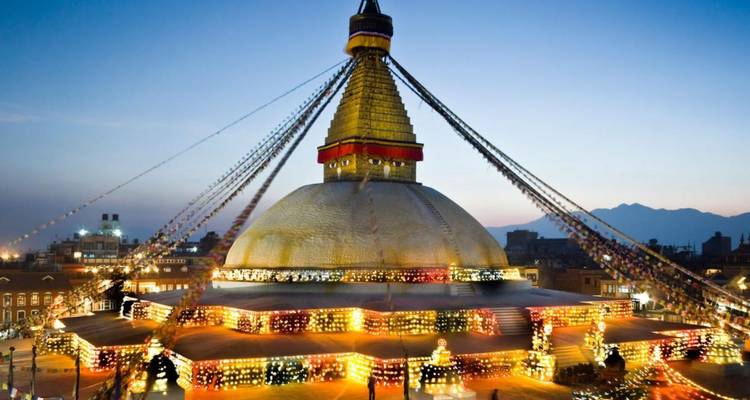 Le Stupa de Boudhanath brillant de mille feux de lampes à beurre au crépuscule contre le ciel qui s'assombrit.