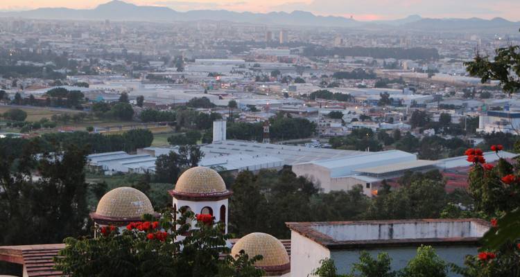 Panorama surélevé d'une ville tentaculaire avec des dômes carrelés et des chaînes de montagnes lointaines à l'aube.