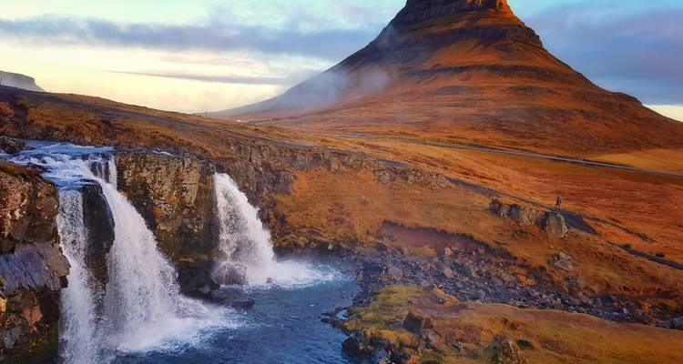 Iconic Kirkjufell mountain highlighted by warm light with twin waterfalls in foreground.