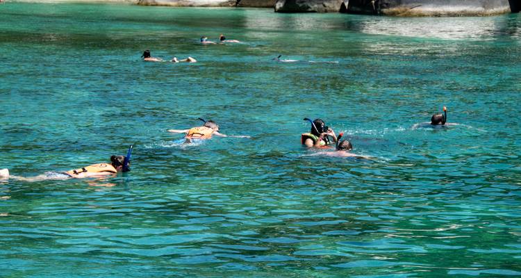 Snorkelers float in crystal-clear turquoise water near rocky outcrops.