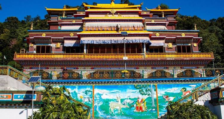 Buntes mehrstöckiges buddhistisches Kloster vor bewaldeten Hügeln.