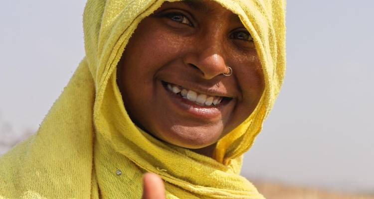 Portrait en gros plan d'une femme souriante enveloppée dans un foulard jaune faisant un signe de pouce levé.
