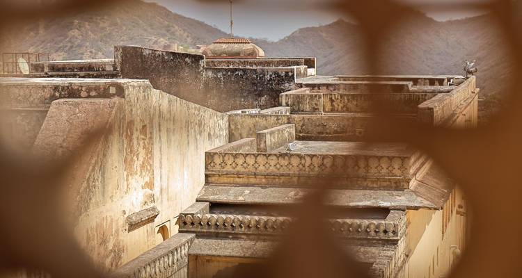 Remparts et terrasses patinés d'un ancien fort vus à travers un écran décoratif avec des collines brumeuses au-delà.