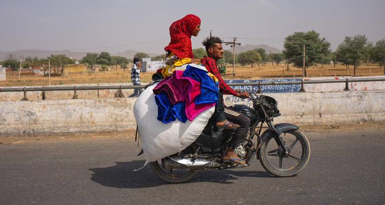 Un homme et un enfant roulent sur une moto chargée de couvertures colorées le long d'une route rurale.