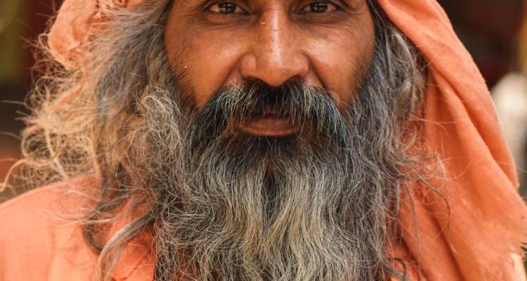 Gros plan d'un homme saint barbu en robes safran regardant vers la caméra.