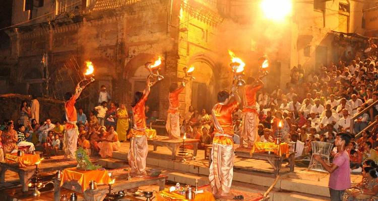 Abend-Ganga-Aarti-Zeremonie in Varanasi mit Priestern, die lodernde Lampen vor einer großen sitzenden Menschenmenge erheben.