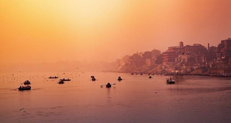 Sanfter goldener Dunst über dem Ganges mit kleinen Ruderbooten verstreut auf dem ruhigen Wasser bei Tagesanbruch.