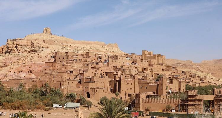 Adobe-Kasbah von Ait Benhaddou erhebt sich über einer Wüstenoase unter blauem Himmel.