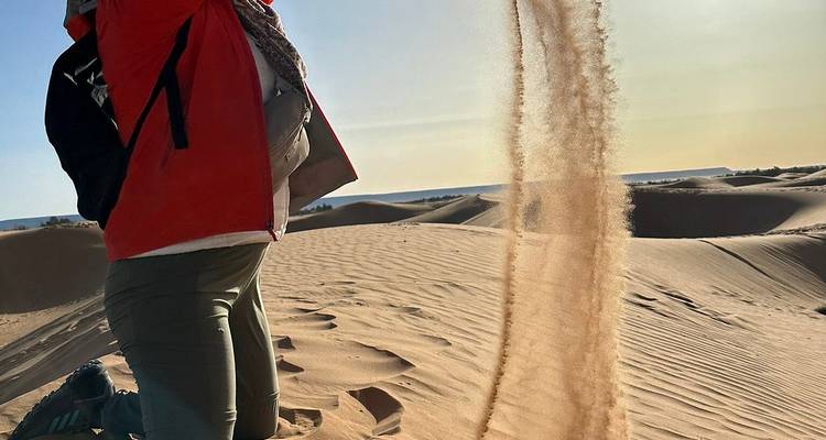 Reisender in roter Jacke wirft eine anmutige Sandwolke auf sonnenbeschienene Dünen.