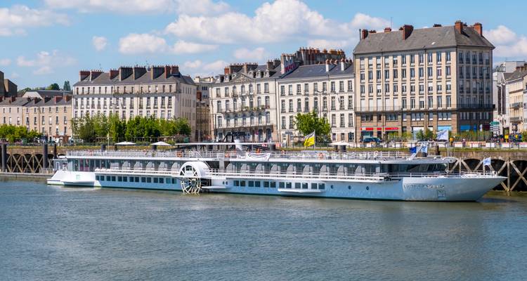 Navire de croisière fluviale moderne amarré le long de bâtiments historiques du front de mer à Nantes.