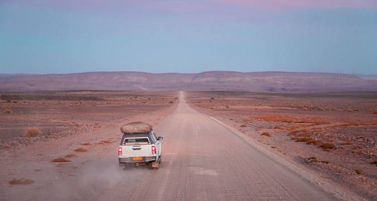 Camionnette roulant sur une route de gravier sans fin à travers un paysage désertique vide au crépuscule.