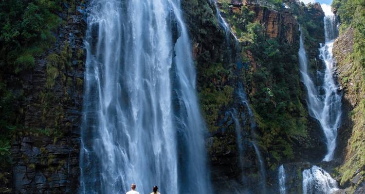 Dos viajeros admiran una alta cascada de doble salto que se precipita por acantilados frondosos