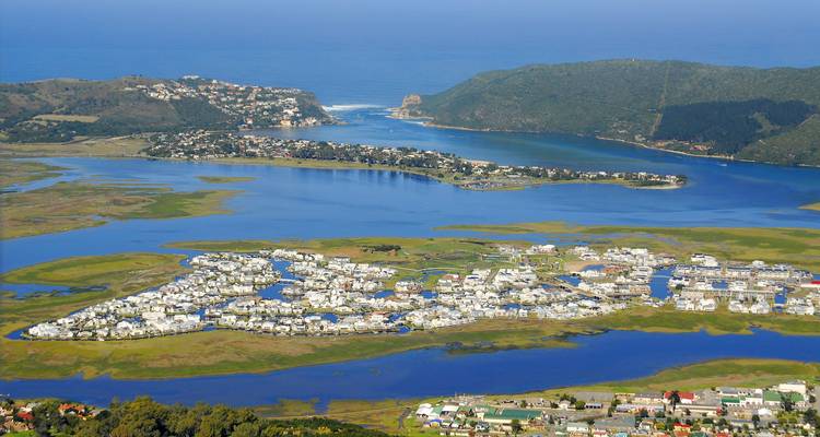 Panorama aéreo de un pueblo de laguna rodeado de colinas verdes y aguas azules del estuario.