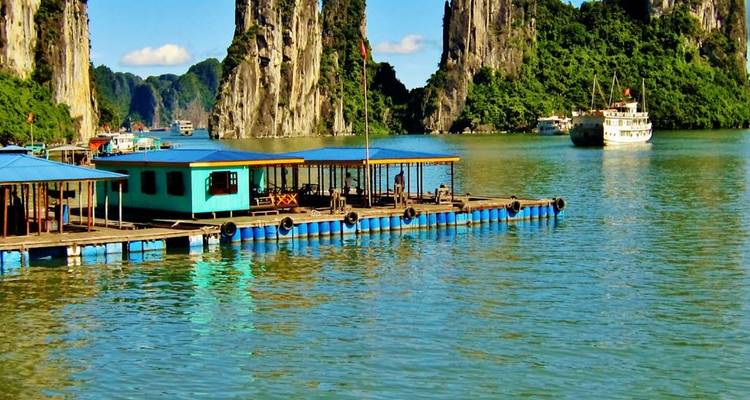 Maisons flottantes et piliers calcaires reflétés dans les eaux jade de la baie d'Halong.