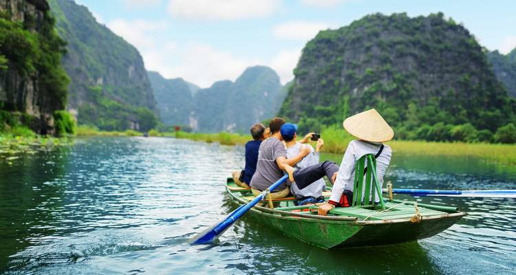 Barque avec des voyageurs glisse le long d'une rivière bordée de falaises calcaires imposantes à Ninh Binh.
