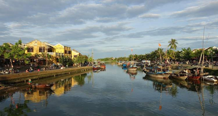 Rive animée de Hoi An avec des bateaux et des maisons historiques illuminées de lanternes sous la lumière du soir.