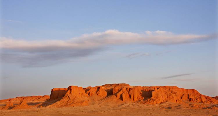 Les falaises de grès orange saisissantes de Bayanzag brillent dans la lumière de fin d'après-midi contre un ciel bleu.