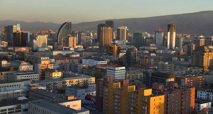 Large paysage urbain d'Oulan-Bator avec des bâtiments modernes et de l'époque soviétique illuminés par la douce lumière du soir, les montagnes faiblement visibles au-delà de l'horizon.