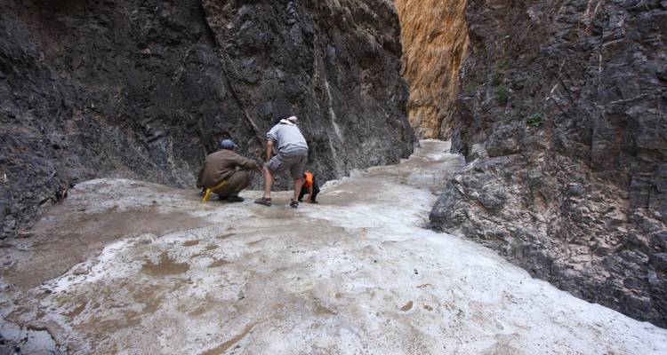 Deux randonneurs s'accroupissent sur un étroit ruisseau gelé à l'intérieur d'une gorge rocheuse escarpée et sombre, examinant la surface de la glace.