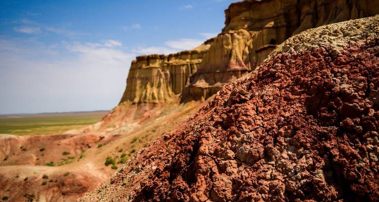 Des falaises sédimentaires aux couleurs vives rouge et jaune s'élèvent au-dessus d'une vaste vallée désertique sous un ciel dégagé.