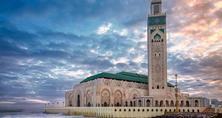 Le minaret imposant de la Mosquée Hassan II se dresse contre un ciel d'aube dramatique au bord de l'océan Atlantique.