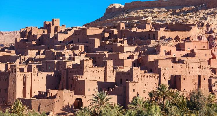Tours de terre et murs d'adobe du village fortifié d'Aït Benhaddou brillant sous un ciel bleu clair.