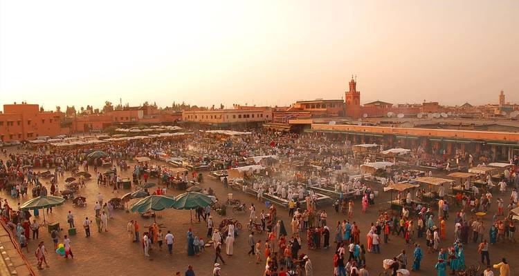 Scène de soirée animée sur la place Jemaa el-Fnaa remplie d'étals de marché, de fumée et de foules dans une brume chaleureuse.