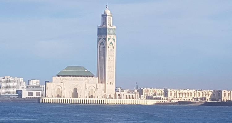 Vue lointaine de la mosquée Hassan II prise depuis la mer avec une eau bleue calme au premier plan.