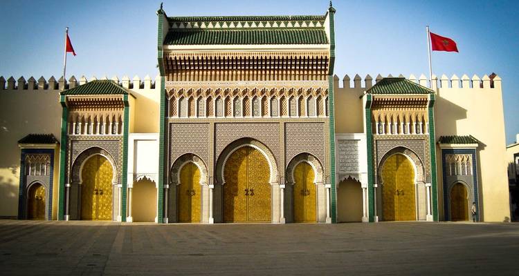 Portes dorées ornées et arches aux tuiles vertes du Palais Royal de Fès encadrées par des drapeaux marocains