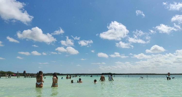 Lagon peu profond aux eaux cristallines avec de nombreux baigneurs debout jusqu'à la taille sous un ciel bleu vif parsemé de nuages.