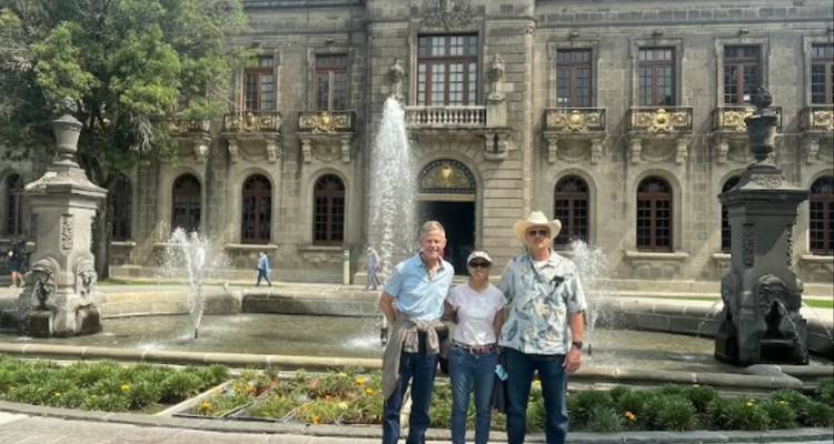 Drei Reisende stehen vor einer barocken Fassade und einem zentralen Brunnen in einem historischen Innenhof in Mexiko-Stadt.
