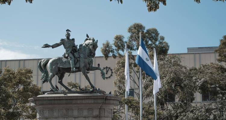 Bronze equestrian statue with El Salvador flag fluttering beside modern buildings