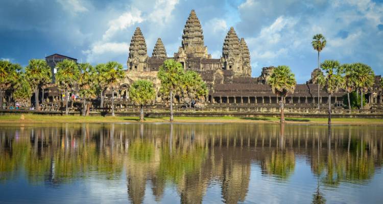 Flèches iconiques d'Angkor Vat parfaitement reflétées dans le bassin de réflexion immobile sous un ciel dramatique.