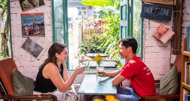 Deux voyageurs partagent des boissons dans un café confortable au style vintage avec des portes ouvertes sur un jardin.