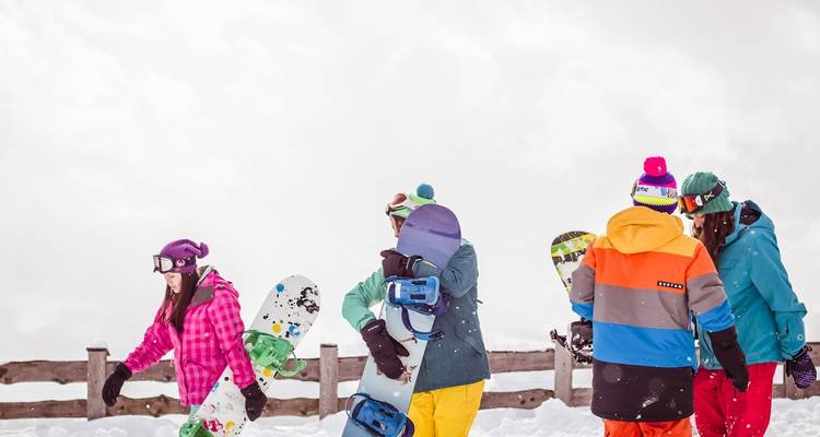 Los snowboarders con equipos coloridos se reúnen en una ladera nevada de la montaña entre copos que caen.