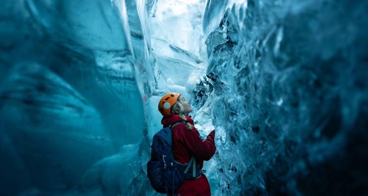 Een klimmer met een helm kijkt omhoog naar glimmende blauwe wanden in een IJslandse ijsgrot.