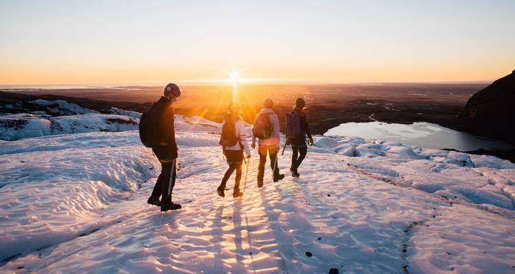 Wandelaars vieren de zonsondergang bovenop een met sneeuw bedekte gletsjer terwijl de zon ondergaat boven de IJslandse kust.