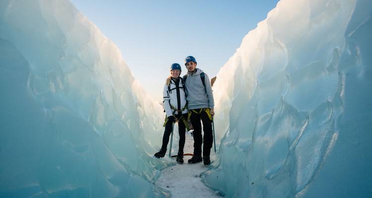 Een koppel in klimuitrusting staat binnen torenhoge ijzige wanden van een smalle gletsjerspleet.