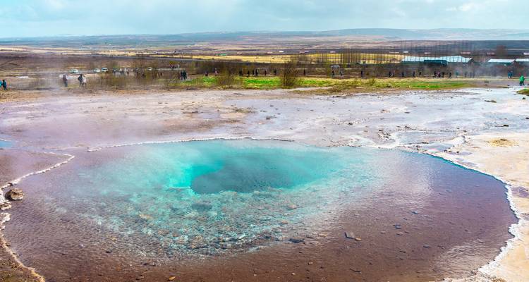 Een dampende aquamarijnblauwe warmwaterbron borrelt in een kleurrijk mineraalbekken in het Geysir geothermische gebied.