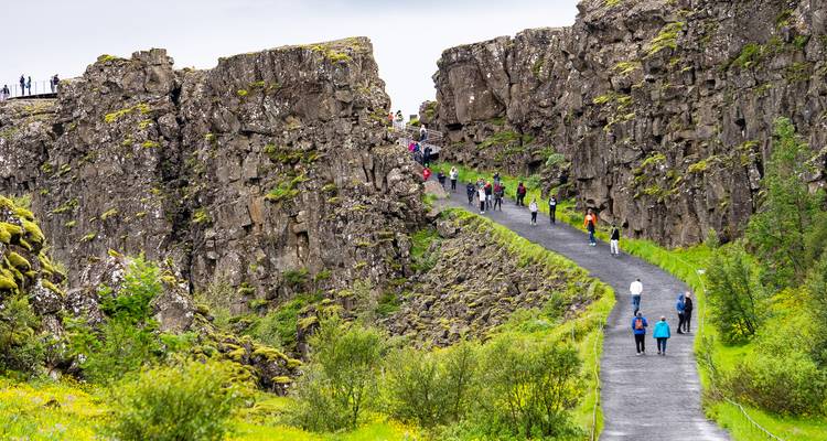 Toeristen wandelen door een dramatische riftvallei van basaltrotsen en groen mos in Nationaal Park Thingvellir.