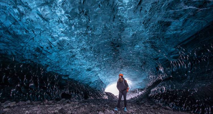 Een eenzame ontdekkingsreiziger met een hoofdlamp staat onder glinsterende blauwe wanden in een enorme gletsjergrot van ijs.