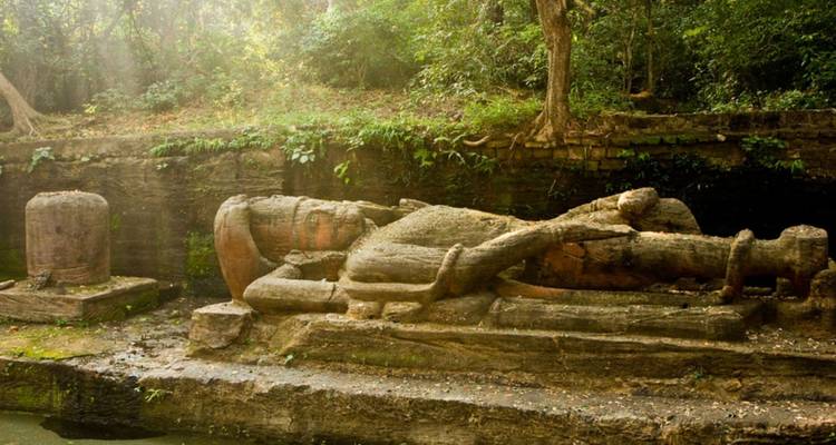Ancient reclining stone idol lies moss-covered in a jungle clearing.