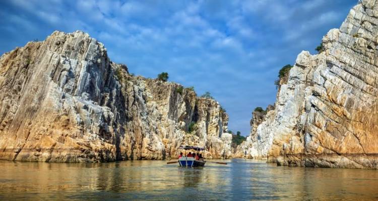 Tour boat glides between towering marble cliffs reflected in calm river water.