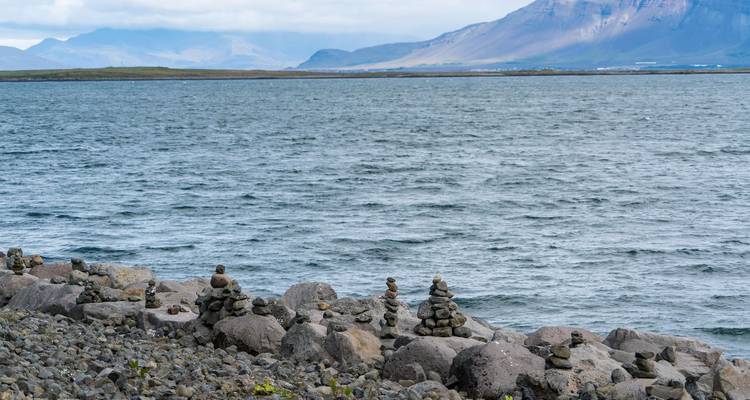 Des cairns de pierre bordent un rivage rocheux surplombant des eaux bleues agitées et des montagnes lointaines.