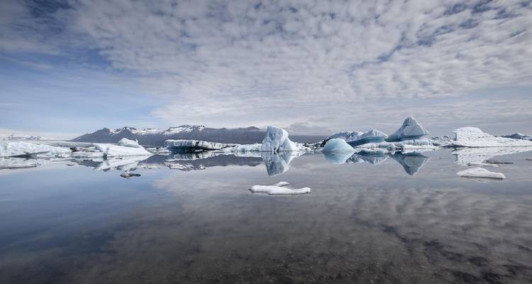 Le lagon au calme miroir reflète les icebergs déchiquetés et le ciel aux motifs nuageux dans une parfaite symétrie.