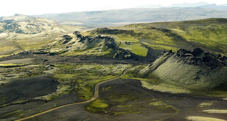 Vue aérienne d'un terrain volcanique couvert de mousse avec un chemin de terre sinueux qui traverse des collines escarpées.