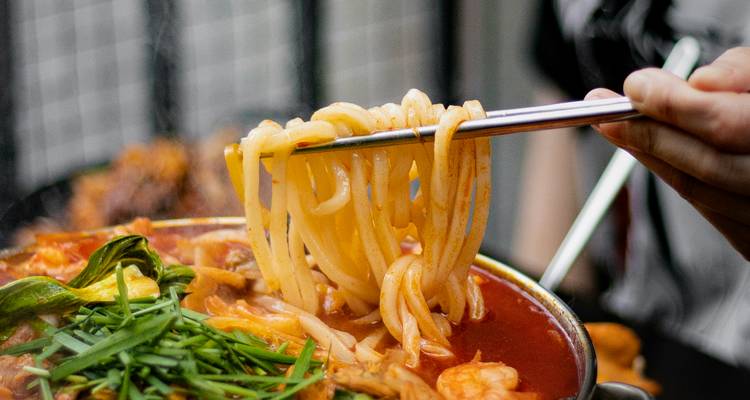 Los palillos levantan fideos goteando con caldo picante de un guiso coreano caliente.