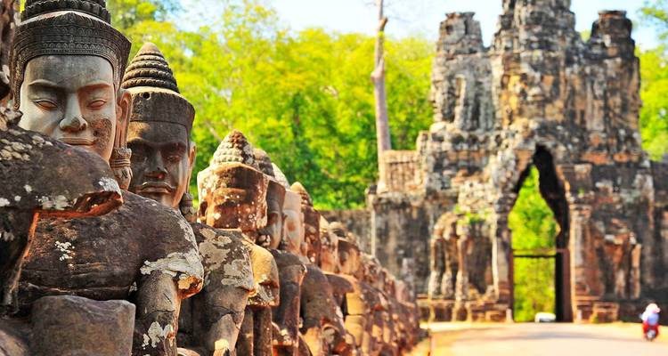 Stenen krijgerstandbeelden staan langs de verhoogde weg naar de sierlijk gebeeldhouwde zuidpoort van Angkor Thom te midden van weelderig groen woud.