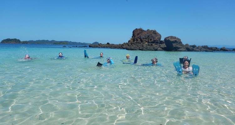 Een vrolijke groep zwemmers met zwemplankjes die spelen in ondiep, kristalhelder lagunewater omringd door rotsachtige eilandjes.