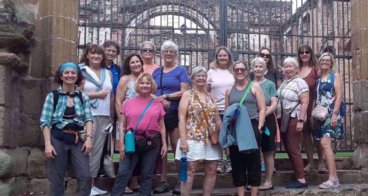 Grote groep vrouwen die poseren voor historische stenen ruïnes met ijzeren hek en boog.